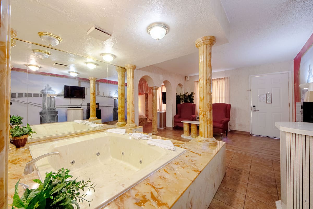 A spacious bathroom with a large bathtub, a vanity with a mirror, and a red armchair.