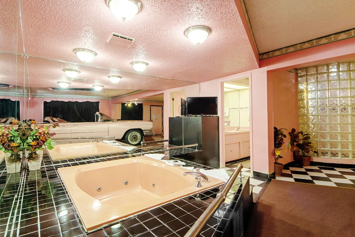 A retro-styled bathroom with a large bathtub, a vintage car, and a television.