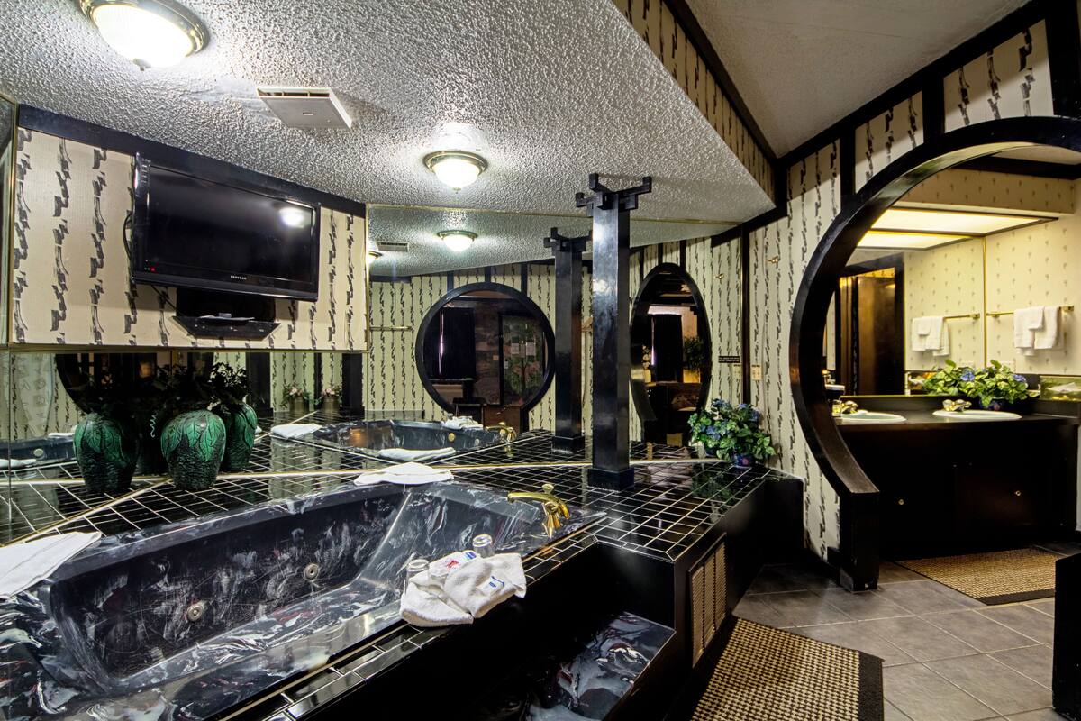 A modern bathroom with a large bathtub, a mirror, and a television mounted on the wall.