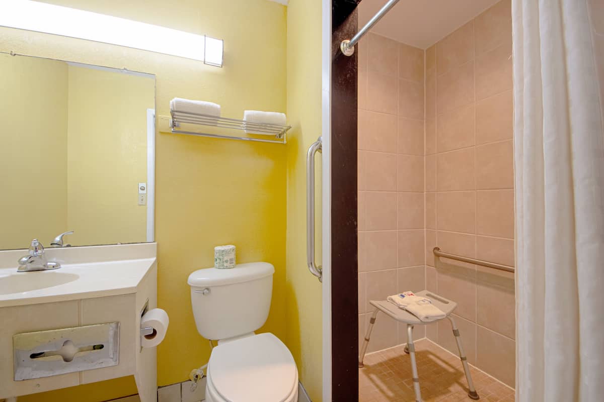 A bathroom with a yellow wall, a white sink, a toilet, and a shower area with a grab bar.