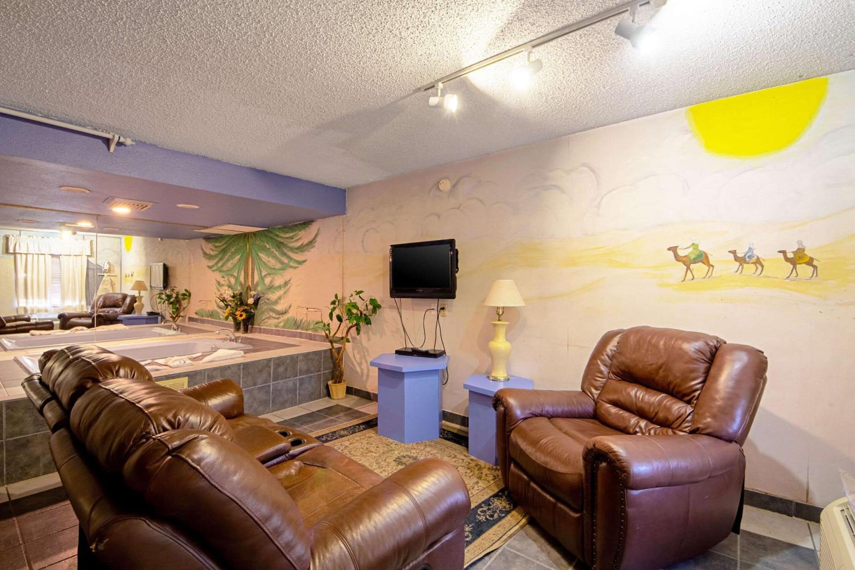 A room with a massage chair, a recliner, a TV, and a wall mural.