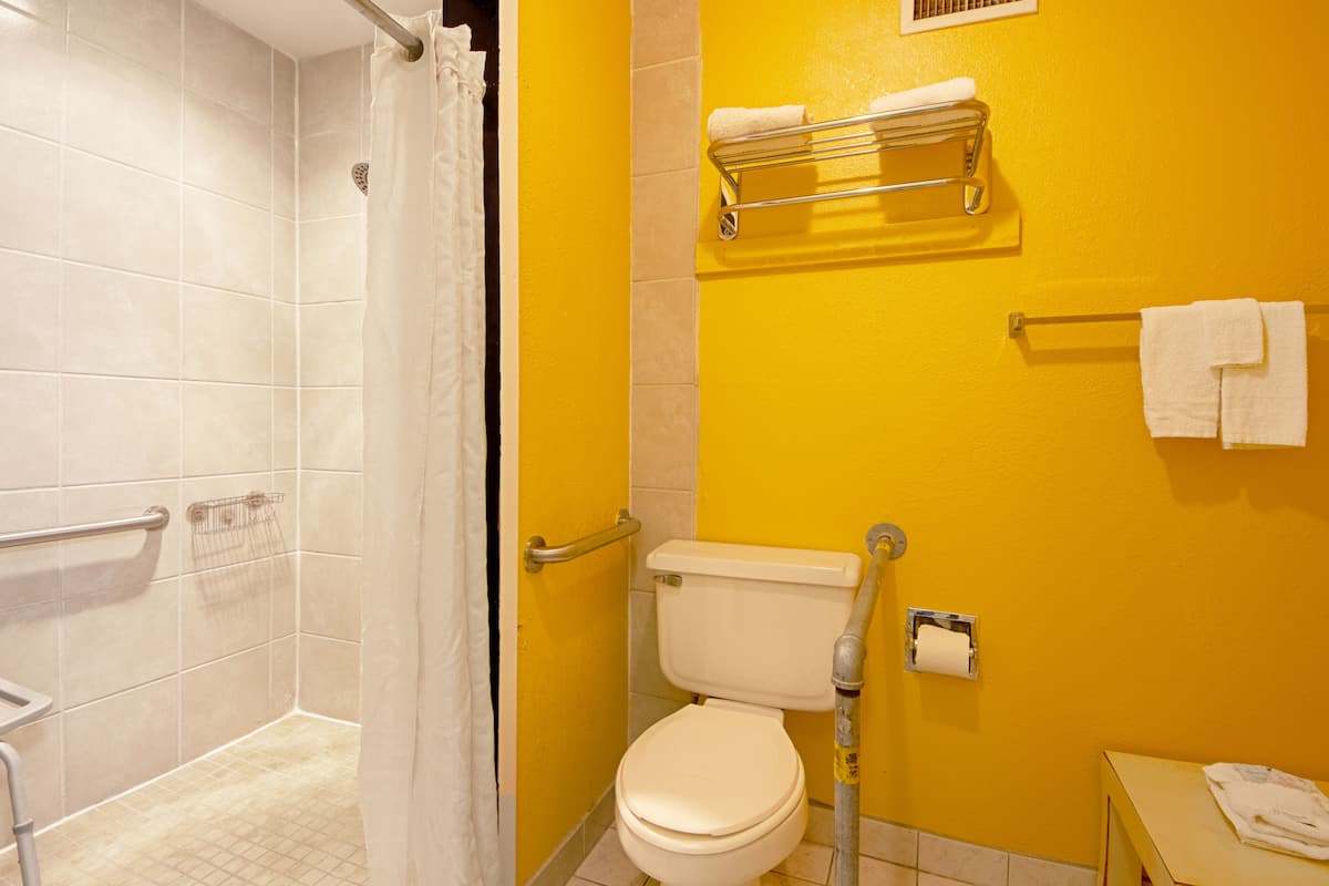 A bathroom with a yellow wall, white toilet, and shower area.