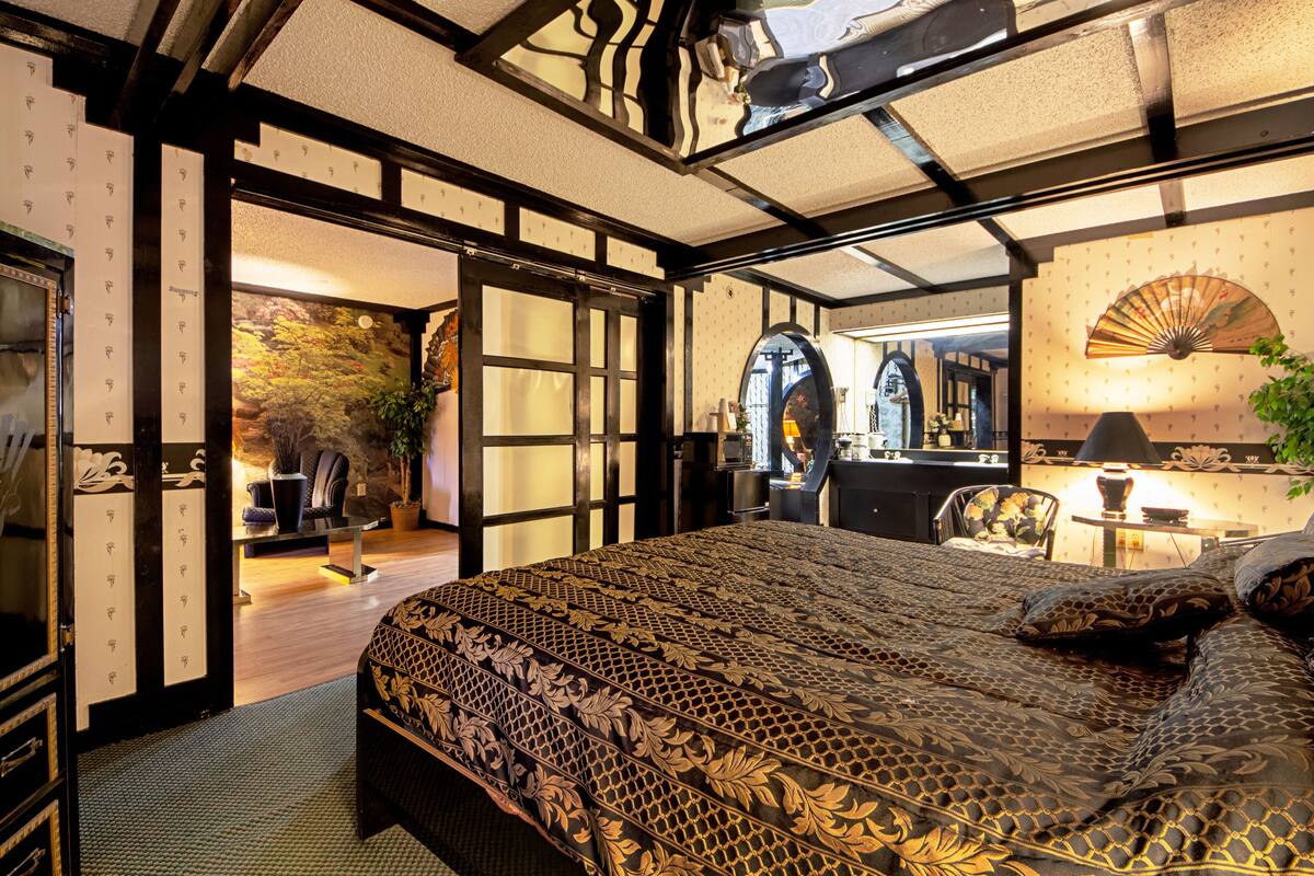 A traditional Japanese-style bedroom with tatami flooring, a low wooden bed, and a sliding door leading to a sitting area with a view of a garden.