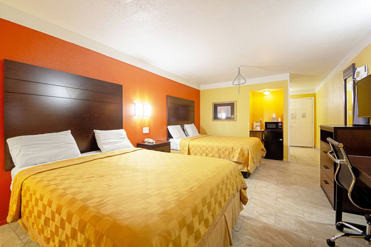 A hotel room with two beds, a desk, a chair, a nightstand, and a small kitchenette.