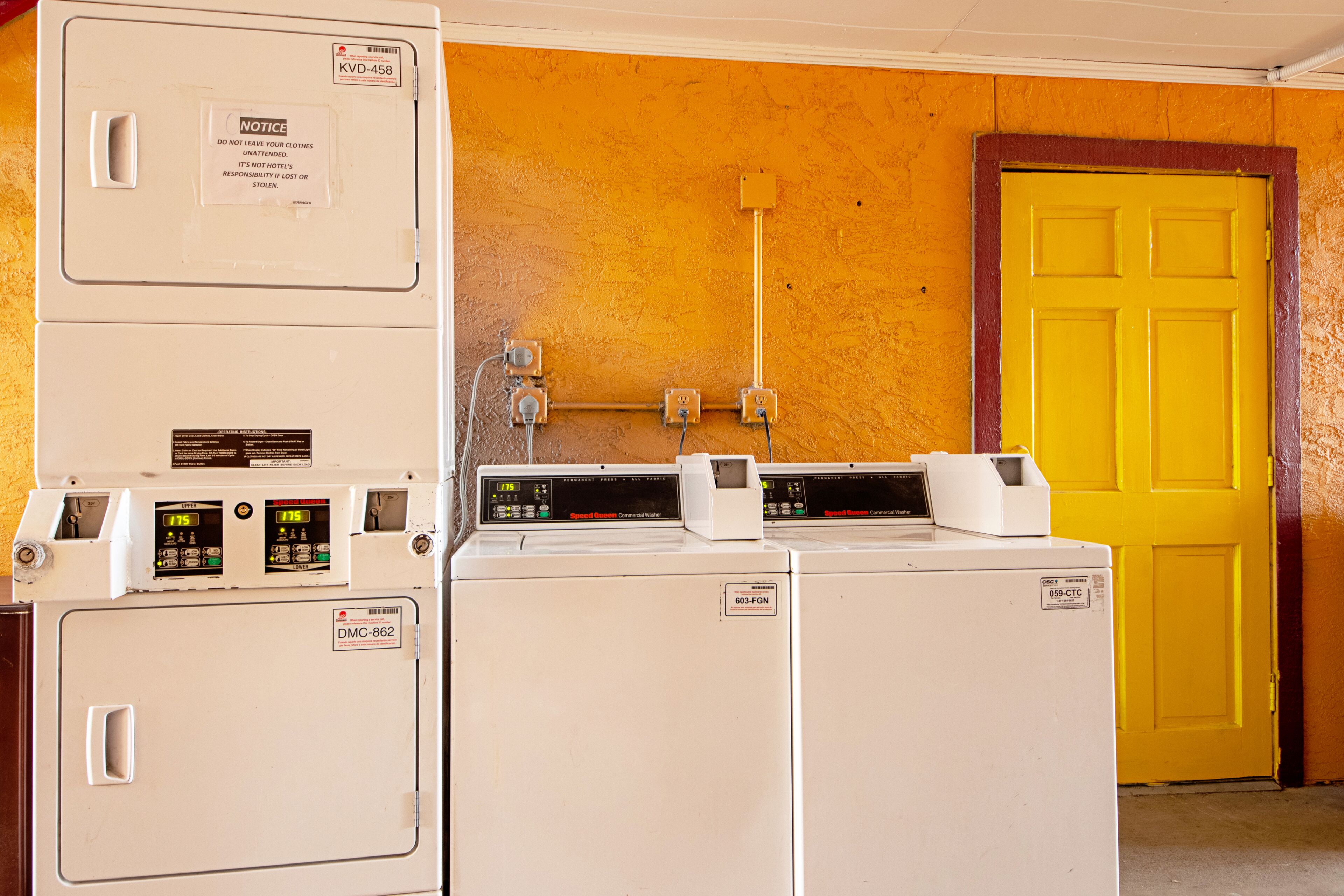 A laundry area with stacked washers and dryers, a yellow door, and visible electrical outlets on the wall.
