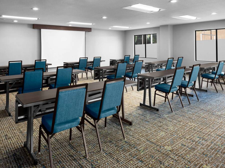 Un salón de conferencias con varias mesas y sillas, una pantalla de proyector y un ventanal grande.