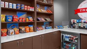 A snack display with various chips and snacks, a refrigerator with beverages, and a 'TRAVEL' sign on the wall.