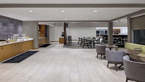 Eine geräumige Hotelhalle mit einem zentral gelegenen Essbereich, einer Küche und einer Sitzecke mit Tischen und Stühlen.