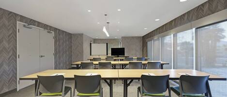A conference room with a large table, several chairs, a television screen, and large windows.