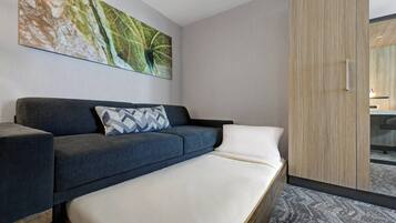 Una habitación de hotel moderna con sofá cama, un cuadro abstracto grande y un armario de madera.