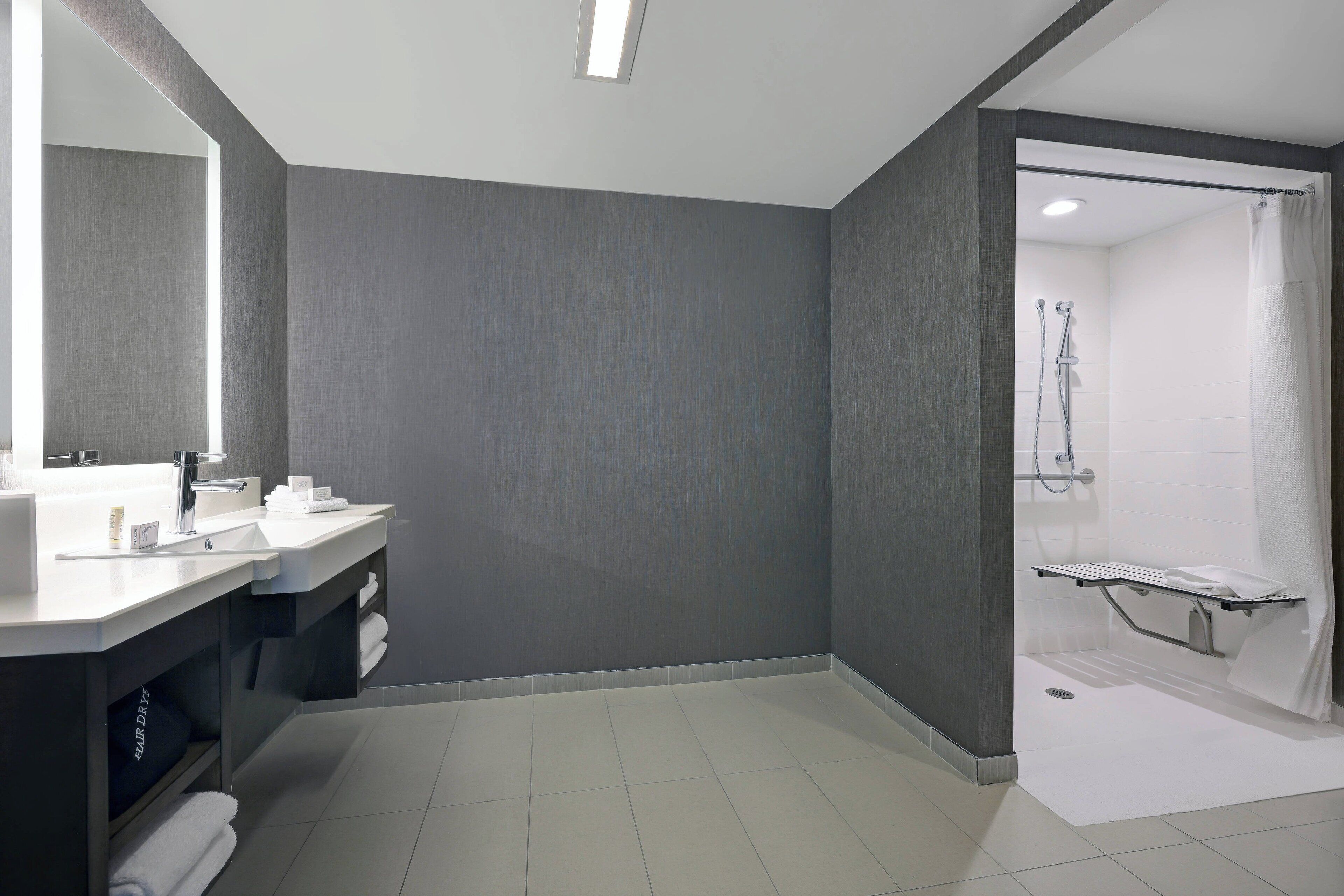 A modern bathroom with a large mirror, two sinks, a shower area, and a towel rack.