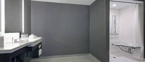 A modern bathroom with a large mirror, two sinks, a shower area, and a towel rack.