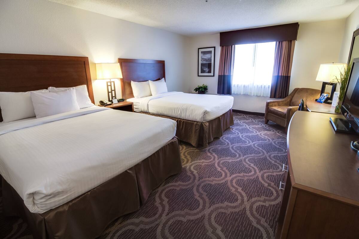 A hotel room with two beds, a desk, a chair, a TV, and a window with curtains.