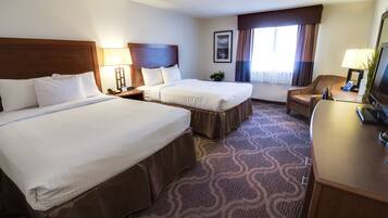 A hotel room with two beds, a desk, a chair, a TV, and a window with curtains.