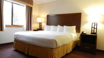 A hotel room with a large bed, two bedside tables with lamps, a window with curtains, and a wooden headboard.