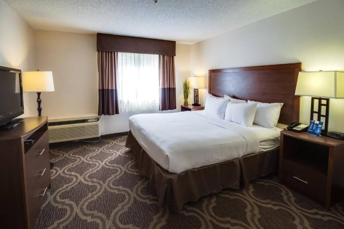 A hotel room with a large bed, a desk with a lamp, a television, and a window with curtains.