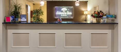 A reception desk with a sign for Ashmore Inn & Suites, a framed award, and a vase with flowers.
