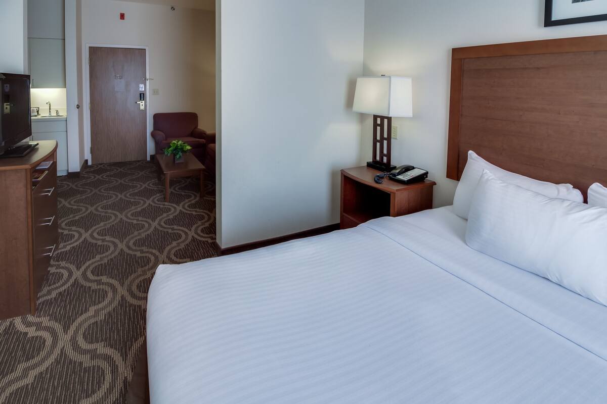 A hotel room with a large bed, a desk with a lamp, a television, and a small seating area.