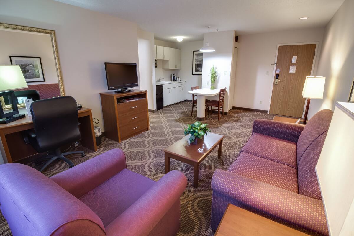 A hotel room with a living area, a kitchenette, a dining table, and a TV.