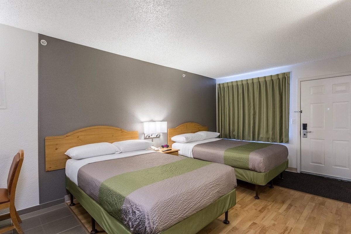 Et hotelværelse med to senge, et træhovedgærde, et natbord, en lampe og en grøn gardin.