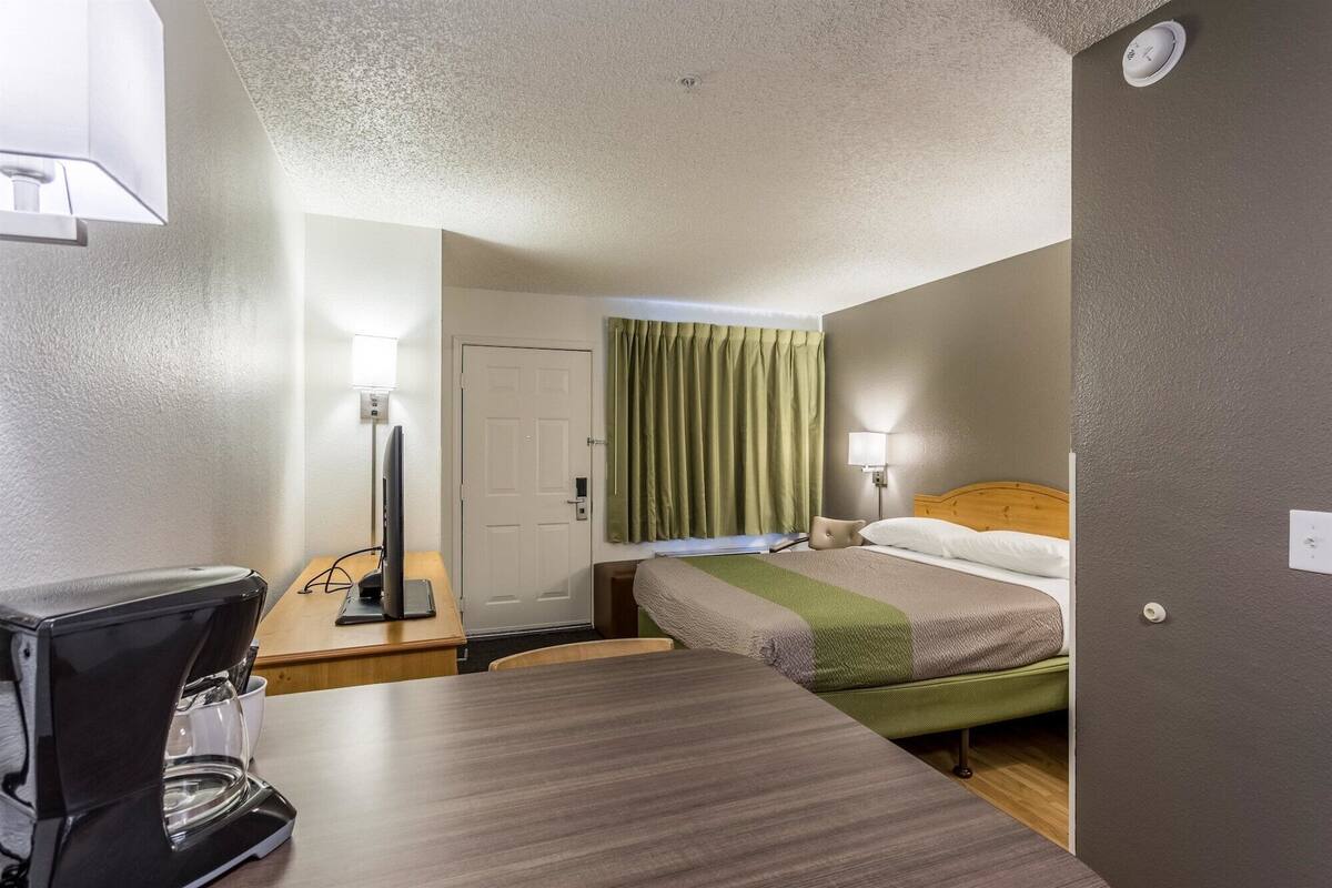 Et hotelværelse med en seng, et skrivebord med kaffemaskine, en lampe og en dør.