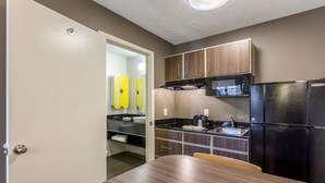 Eine kompakte Küche mit Mikrowelle, Herd und Kühlschrank. Ein Esstisch mit Stühlen ist zu sehen.