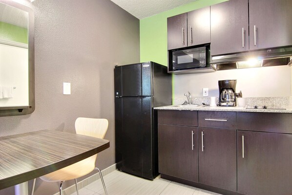 A compact kitchen with dark cabinets, a black refrigerator, a microwave, and a coffee maker.