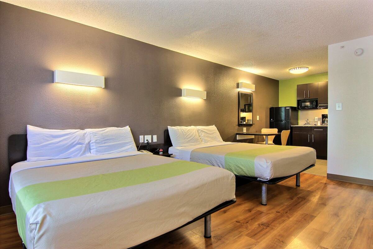 A hotel room with two beds, a kitchenette, and a bathroom.