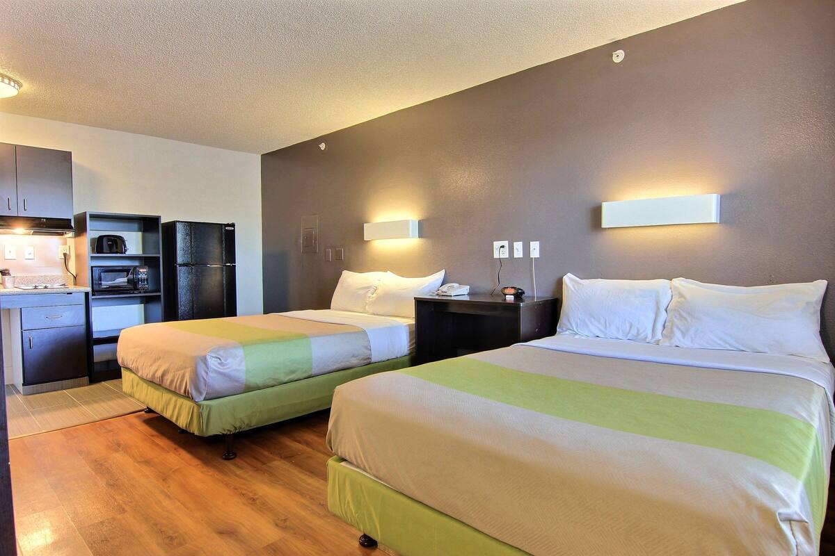 A hotel room with two beds, a kitchenette, and a bathroom.