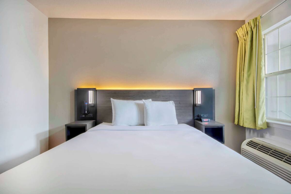 Ein Hotelzimmer mit einem großen Bett, zwei Nachttischen mit Lampen, einem Fenster mit Vorhängen und einem Wandheizkörper.