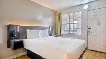 A hotel room with a large bed, bedside tables, a nightstand, a window with curtains, and a door.