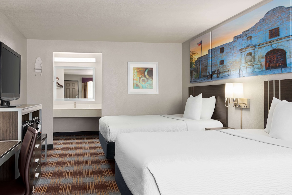 A hotel room with two beds, a desk, a TV, a painting, and a window.