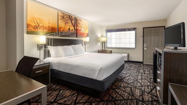 Ein Hotelzimmer mit Bett, Schreibtisch, Fernseher und einem Kunstwerk an der Wand.