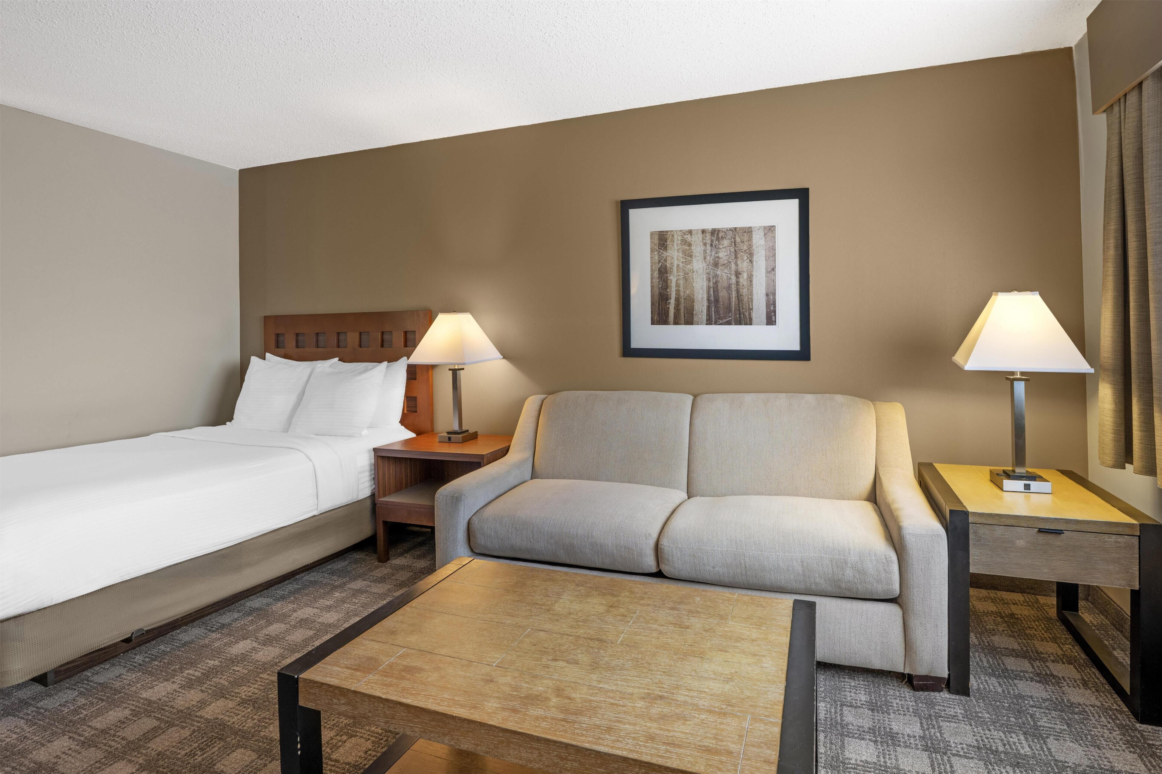 Una habitación de hotel con cama, sofá, mesa de centro y dos lámparas de noche.