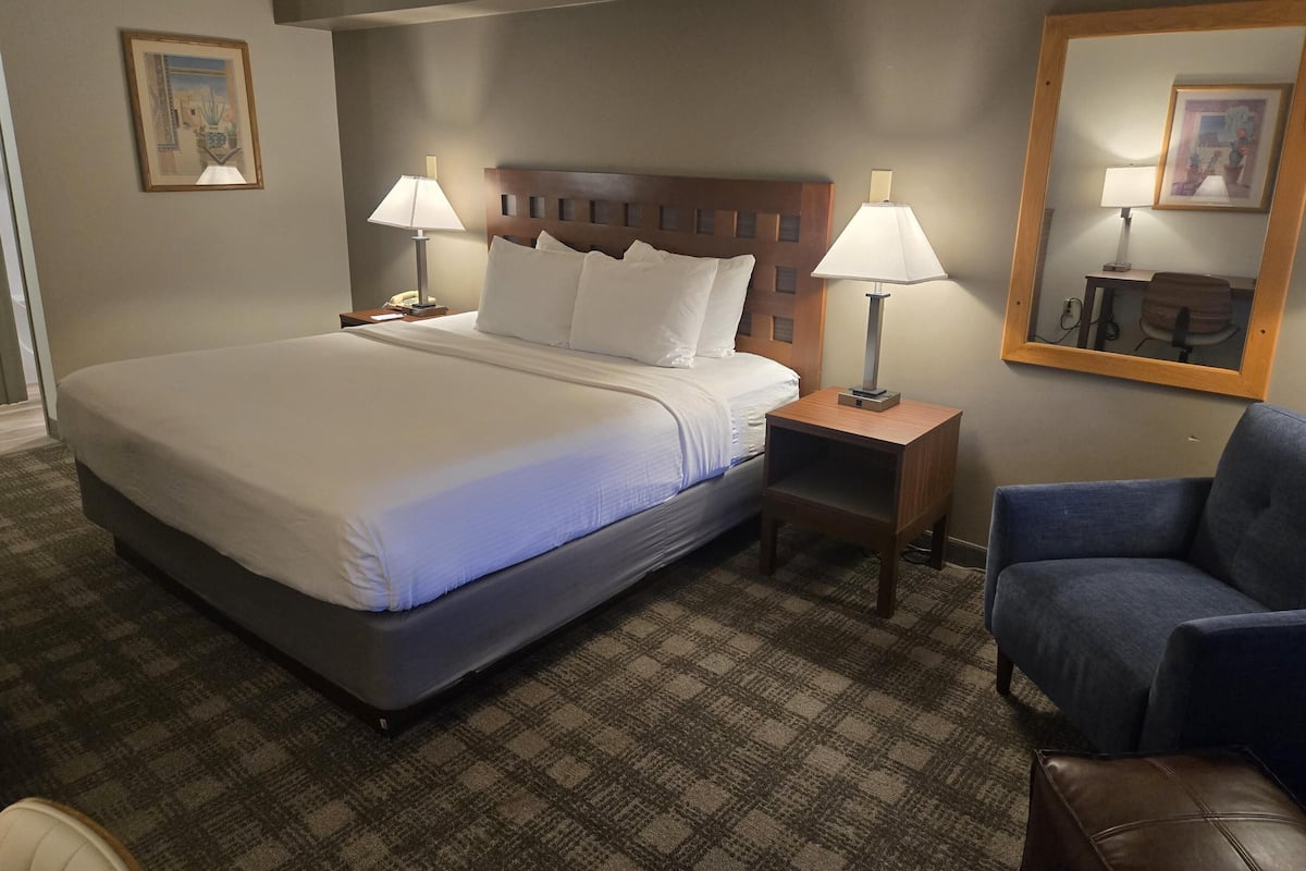 A hotel room with a large bed, two bedside tables with lamps, a chair, and a mirror on the wall.