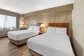 Ein Hotelzimmer mit zwei Betten, einem fensterbelaubten Fenster, einem Schreibtisch mit Lampe und einem Wandheizkörper.