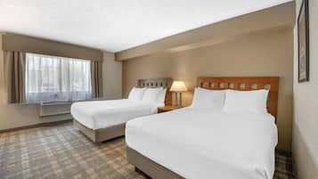 Quarto de hotel com duas camas, uma janela com cortinas, ar condicionado fixado na parede e um tapete estampado.