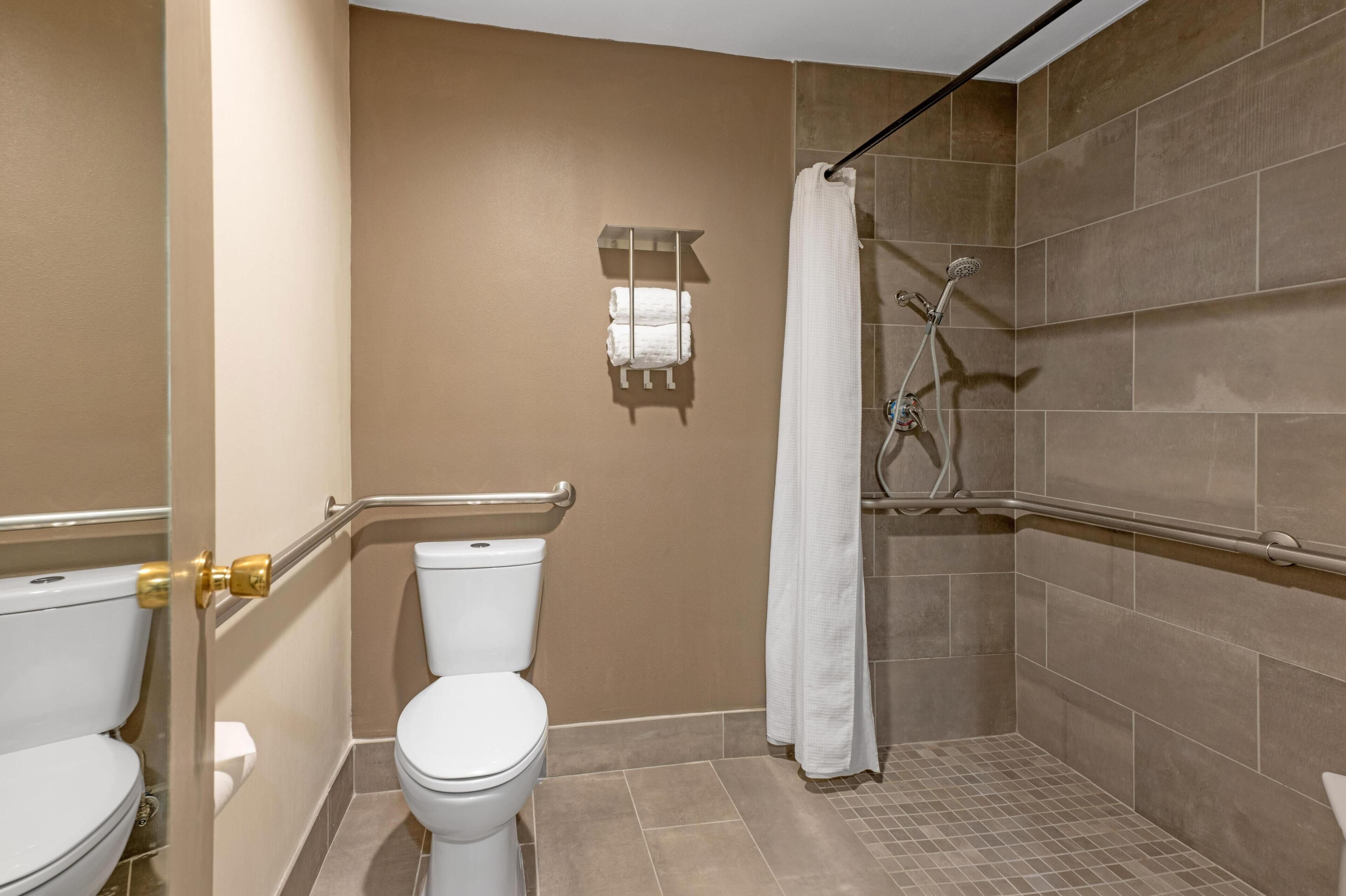 Un baño con inodoro, ducha con cabezal de ducha manual y barra para toallas.