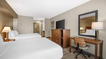 A hotel room with two beds, a desk with a chair, a dresser, a television, and a mirror.