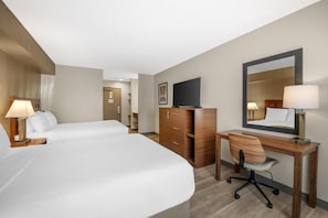 A hotel room with two beds, a desk with a chair, a dresser, a television, and a mirror.