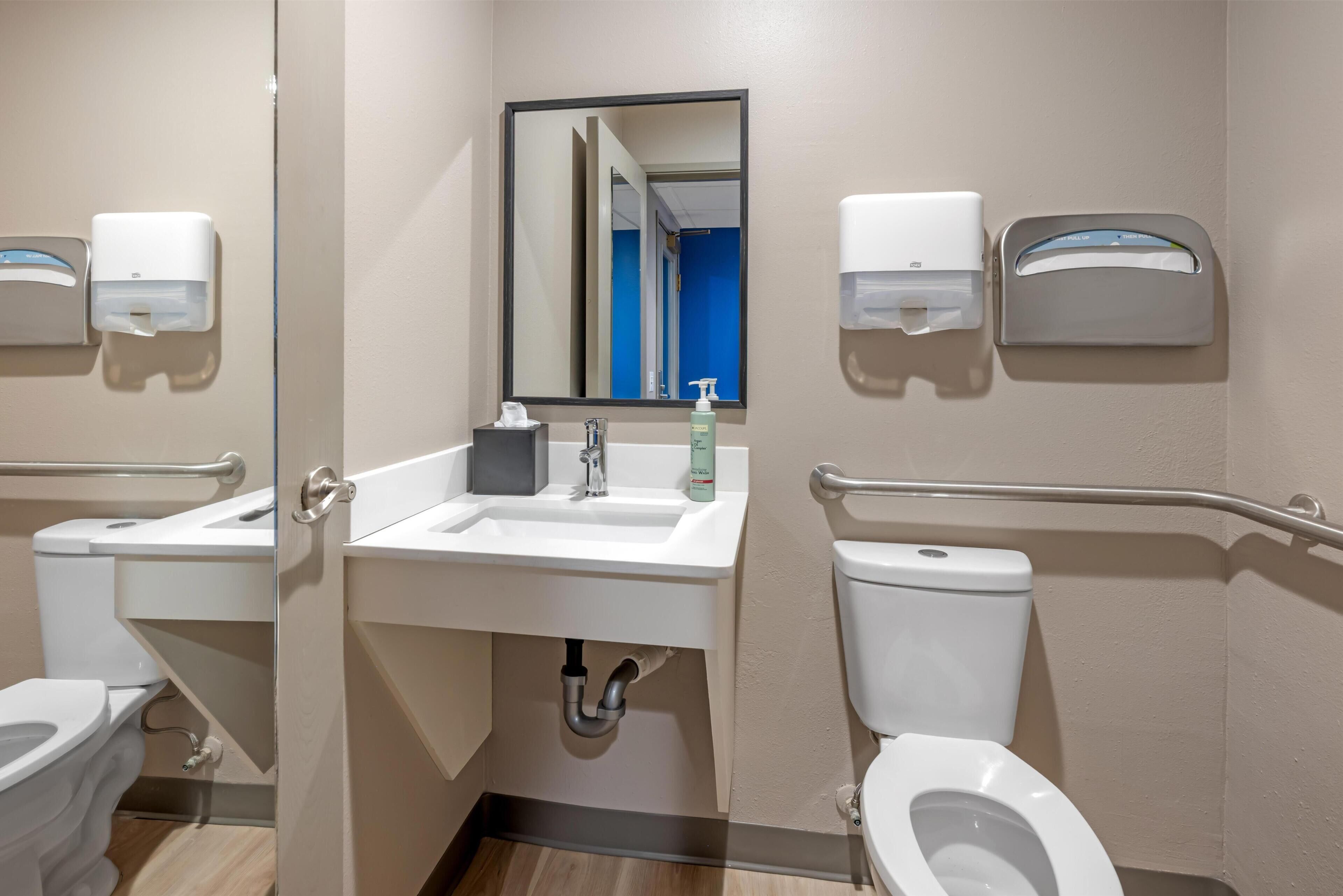 Et standard badeværelse med håndvask, spejl, toilet og håndtørrer.