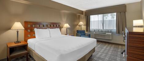 A hotel room with a large bed, two bedside lamps, a chair, a desk, and a large window with curtains.