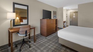 Une chambre d’hôtel comprenant un lit, un bureau avec une chaise, une commode, un téléviseur et une porte.