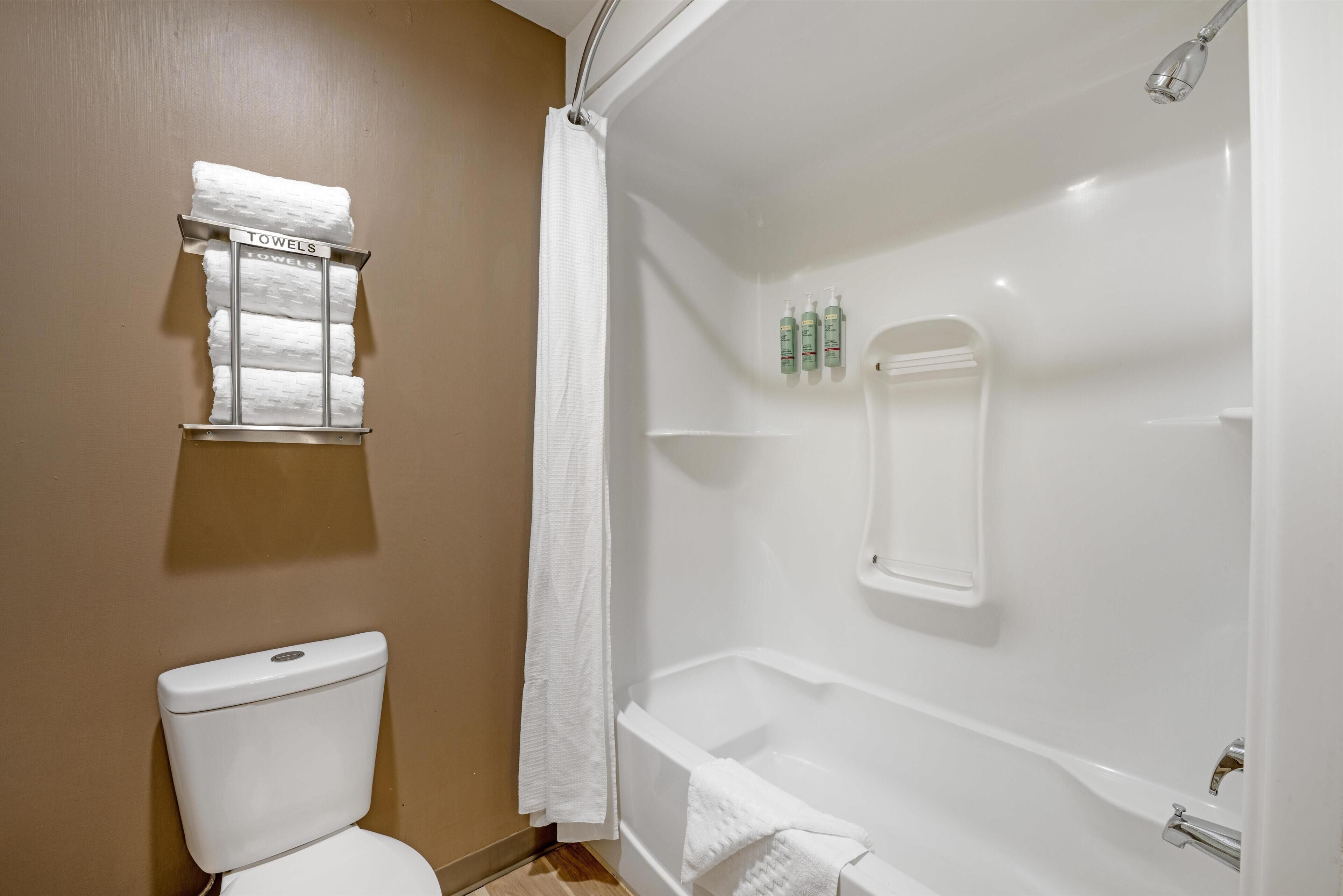 Un baño con inodoro, ducha con puerta de vidrio y toallero con toallas.