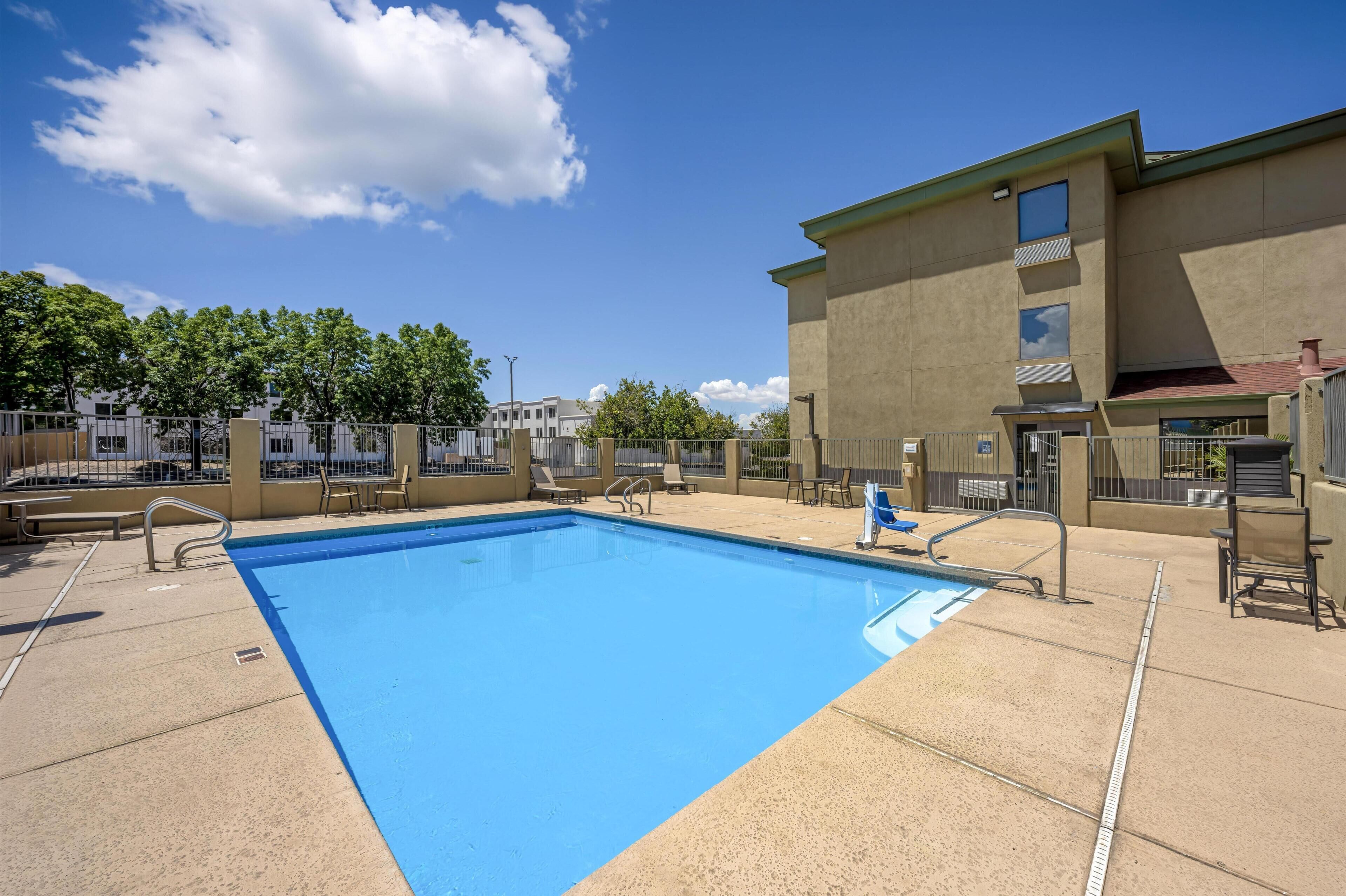 Piscina com superfície de água azul cristalina, rodeada por um deck de concreto com grades de metal e cadeiras de sol.