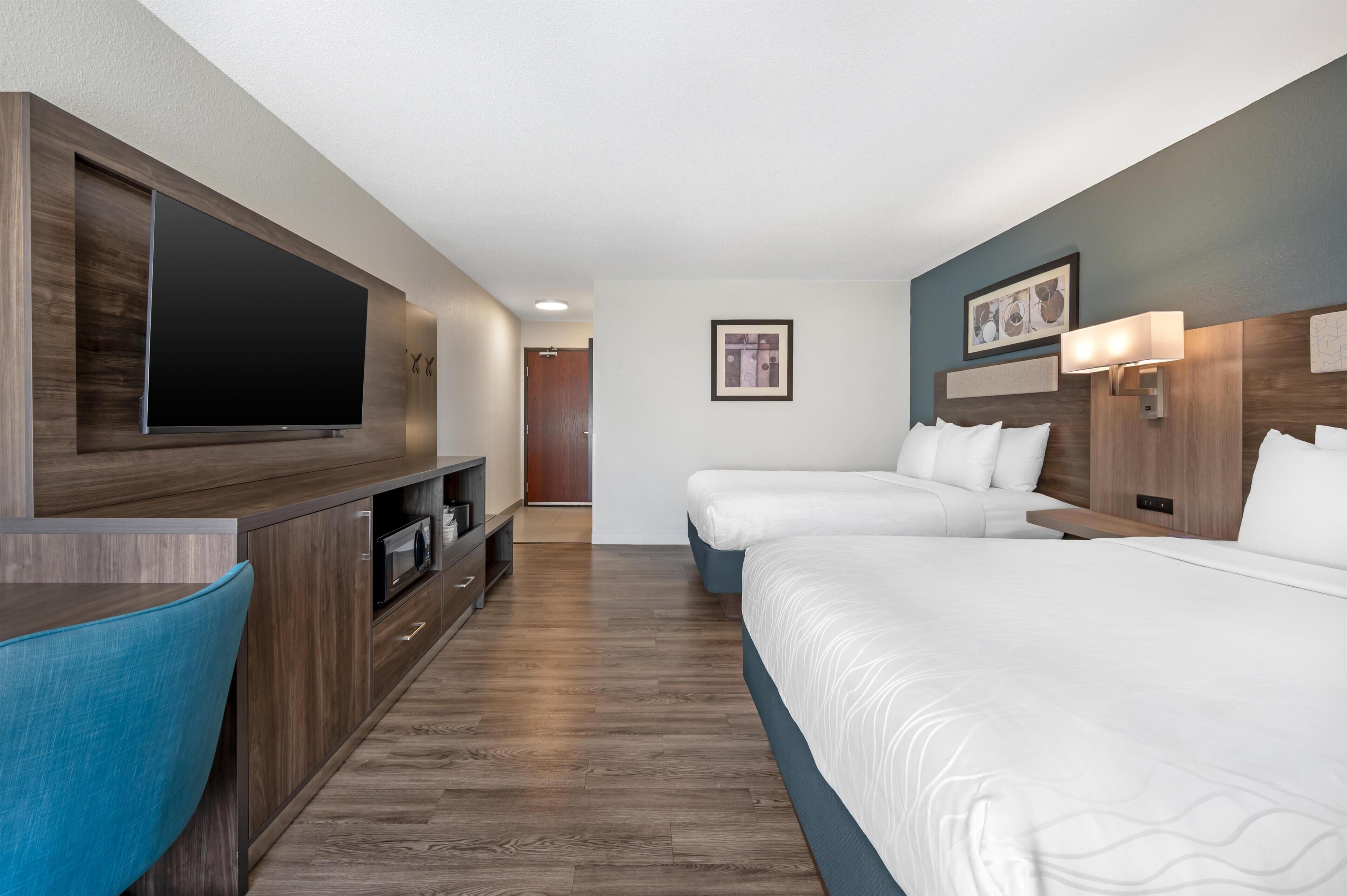 A hotel room with a TV, two beds, a desk, and a chair.