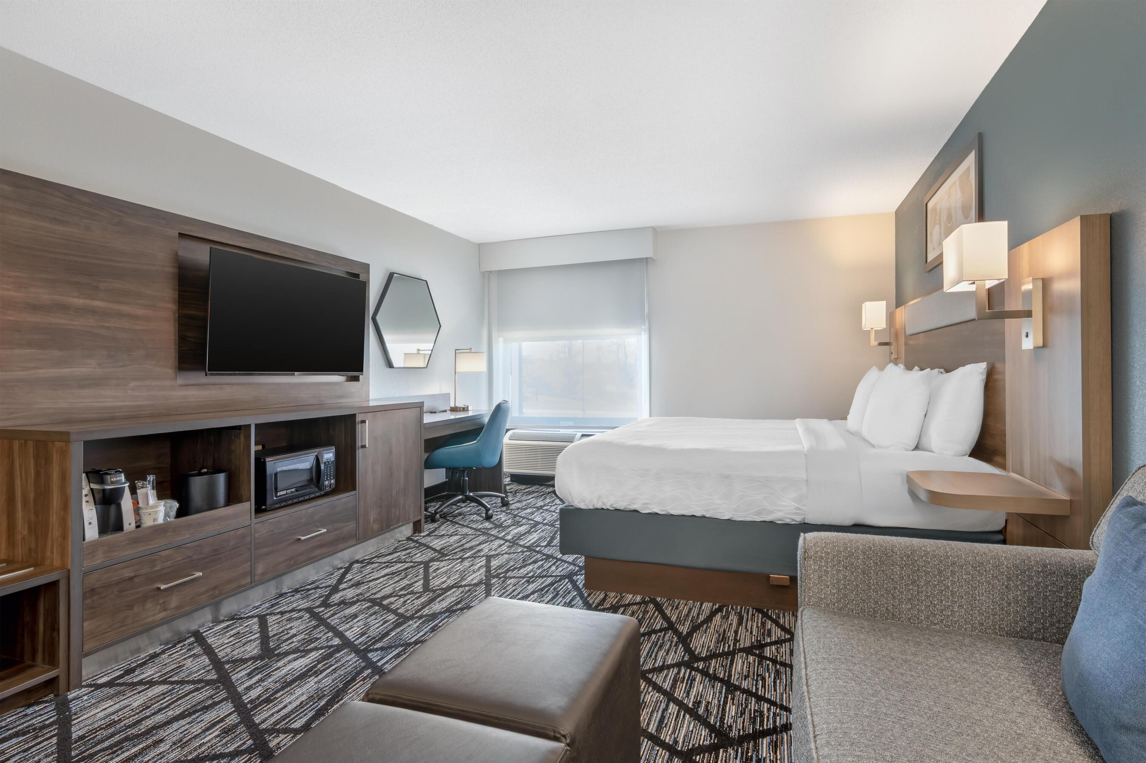 A hotel room with a bed, a desk, a television, a chair, and a sofa.