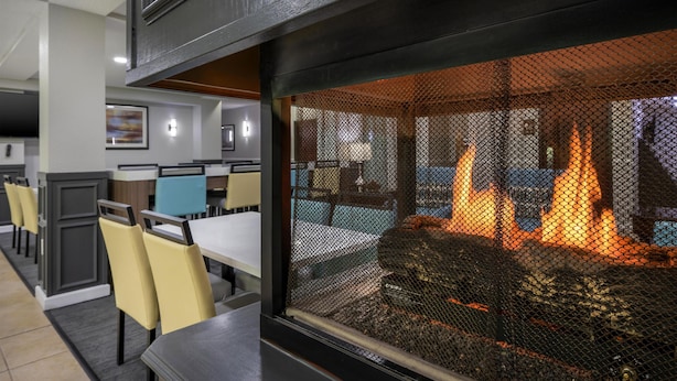 Un restaurante con una chimenea, mesas para comer, sillas y vistas a través de una celosía.