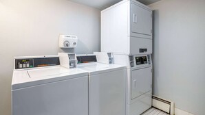 Un espace buanderie comprenant trois machines à laver et trois sèche-linge superposés, un distributeur de lessive et un panneau de commande.