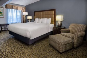 A hotel room with a large bed, two bedside tables with lamps, a chair, and a desk.